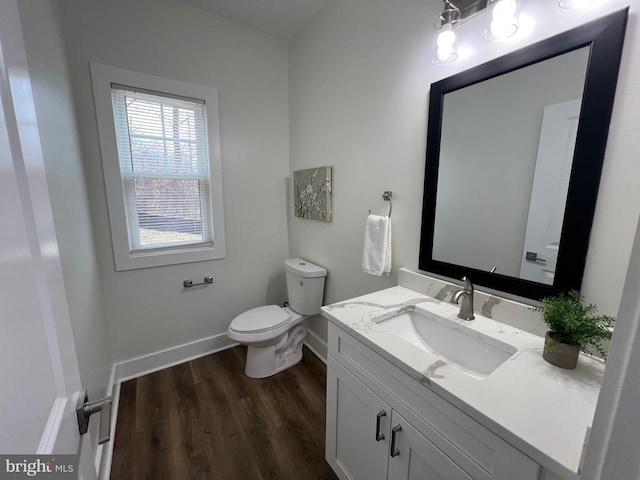 half bathroom featuring toilet, vanity, baseboards, and wood finished floors