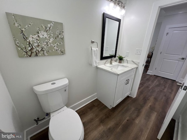 half bath with toilet, vanity, baseboards, and wood finished floors