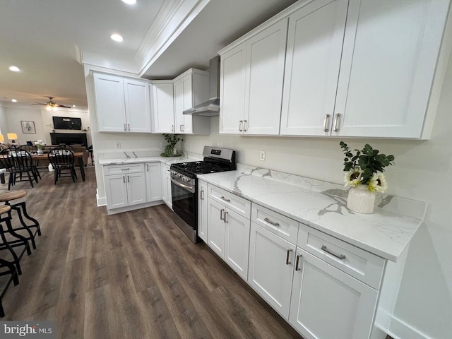 kitchen featuring dark wood-type flooring, a ceiling fan, gas stove, wall chimney exhaust hood, and white cabinets