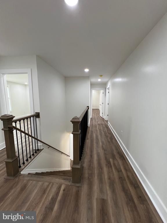 hall featuring an upstairs landing, dark wood-style floors, recessed lighting, and baseboards