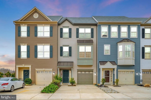 townhome / multi-family property featuring a garage, metal roof, driveway, and a standing seam roof