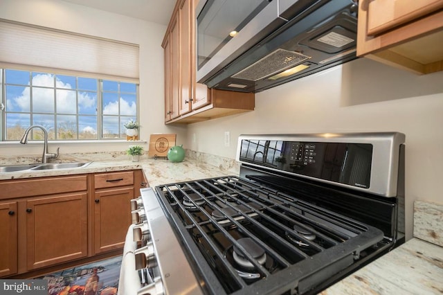 kitchen featuring ventilation hood, light stone countertops, appliances with stainless steel finishes, brown cabinetry, and a sink