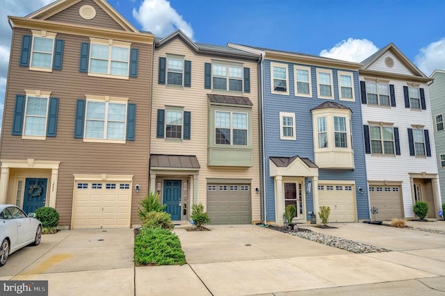 townhome / multi-family property with a standing seam roof, an attached garage, driveway, and metal roof