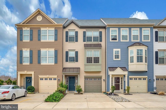 townhome / multi-family property with metal roof, an attached garage, driveway, and a standing seam roof