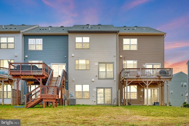 rear view of property with a deck, central AC unit, stairway, and a lawn