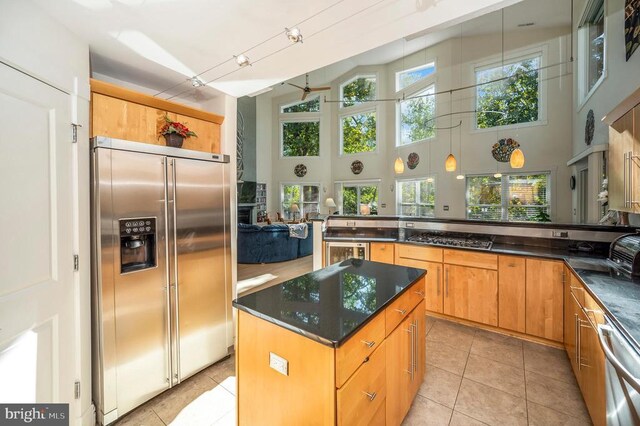 kitchen featuring appliances with stainless steel finishes, a high ceiling, a center island, light tile patterned floors, and kitchen peninsula