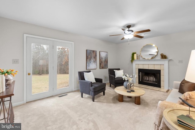 living room with ceiling fan, carpet flooring, visible vents, baseboards, and a tiled fireplace