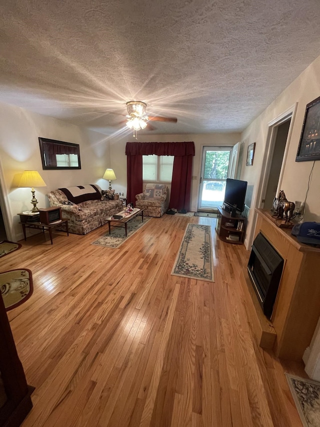 bedroom with ceiling fan, a stone fireplace, a textured ceiling, and light wood-type flooring