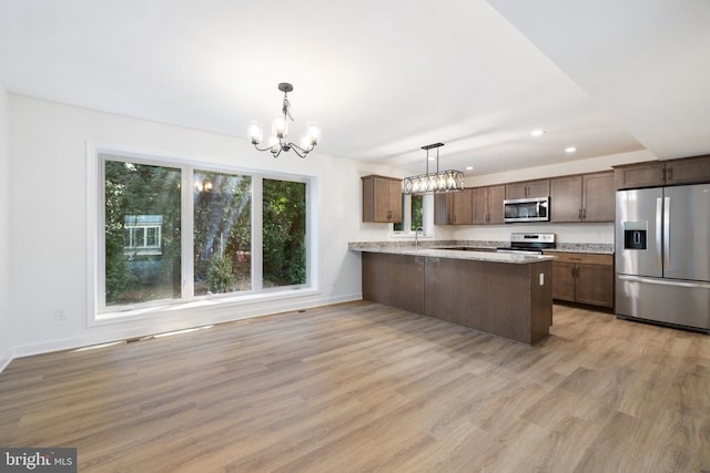 kitchen featuring light hardwood / wood-style flooring, appliances with stainless steel finishes, kitchen peninsula, a notable chandelier, and pendant lighting