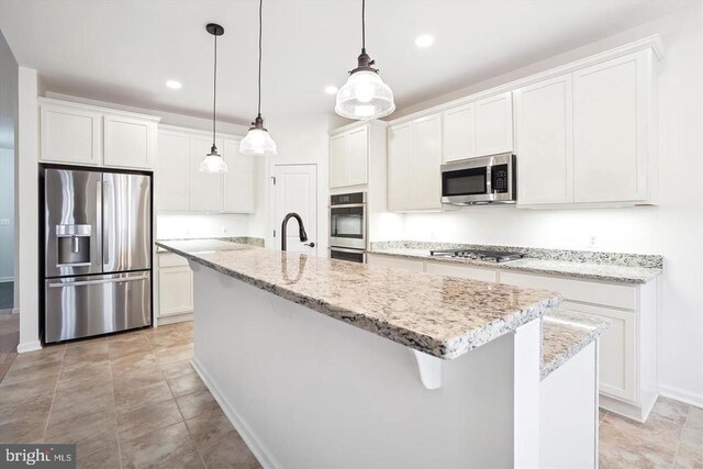 kitchen with appliances with stainless steel finishes, hanging light fixtures, light stone countertops, white cabinets, and a center island with sink