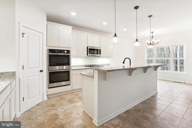 kitchen featuring a breakfast bar, white cabinetry, stainless steel appliances, light stone countertops, and a center island with sink