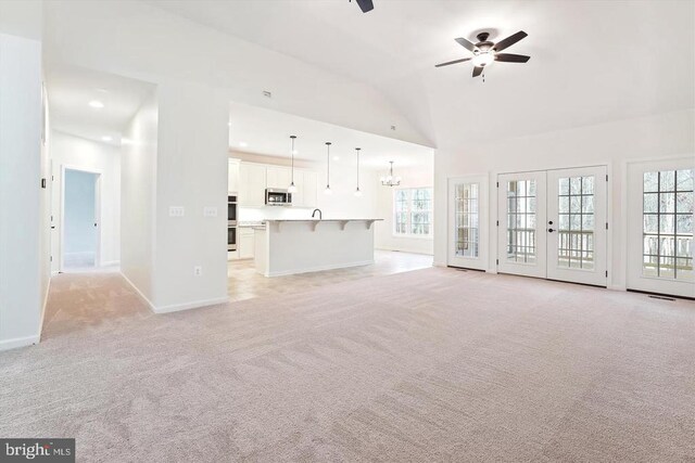 unfurnished living room with french doors, plenty of natural light, ceiling fan with notable chandelier, and light carpet