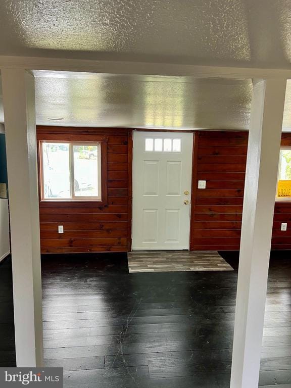 entryway featuring dark wood-type flooring, wooden walls, and a textured ceiling