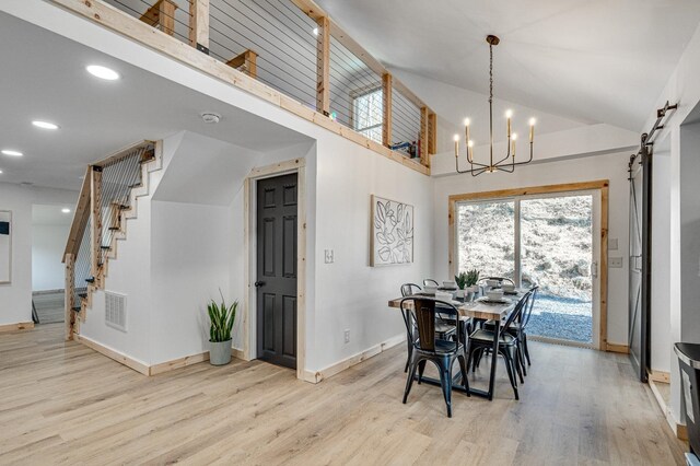 dining space featuring high vaulted ceiling, a barn door, a chandelier, and light hardwood / wood-style floors