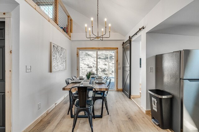 dining room featuring lofted ceiling, a notable chandelier, light hardwood / wood-style floors, and a barn door