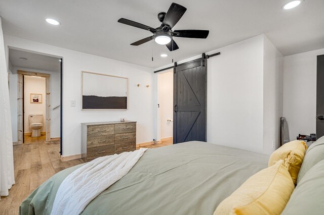 bedroom featuring ceiling fan, ensuite bathroom, a barn door, and light wood-type flooring