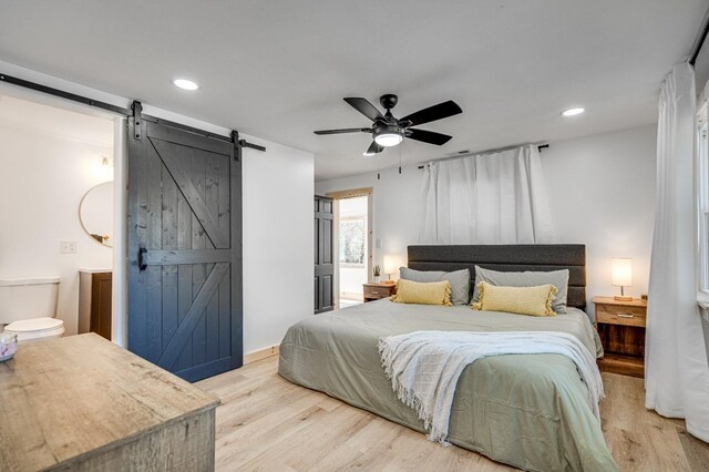 bedroom featuring connected bathroom, a barn door, ceiling fan, and light wood-type flooring