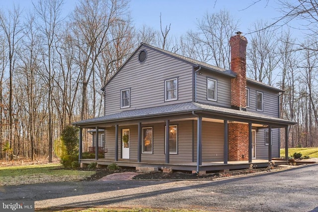 farmhouse with a shingled roof, covered porch, and a chimney