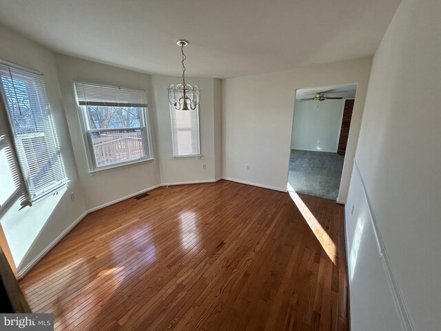 unfurnished dining area featuring dark hardwood / wood-style flooring and ceiling fan with notable chandelier