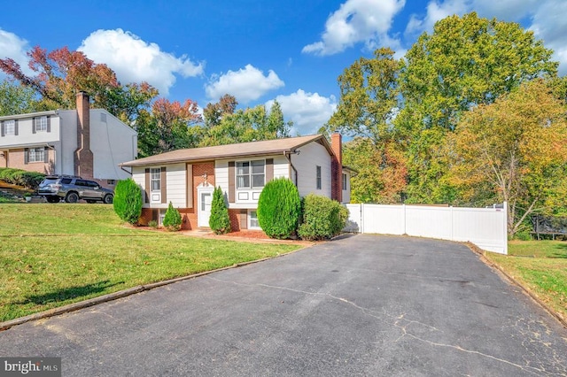 split foyer home with a front yard, fence, brick siding, and a chimney