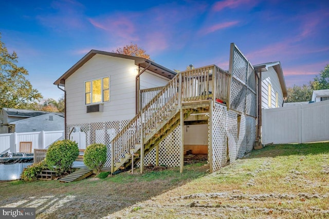 back of house at dusk featuring a wooden deck, a yard, stairs, and fence