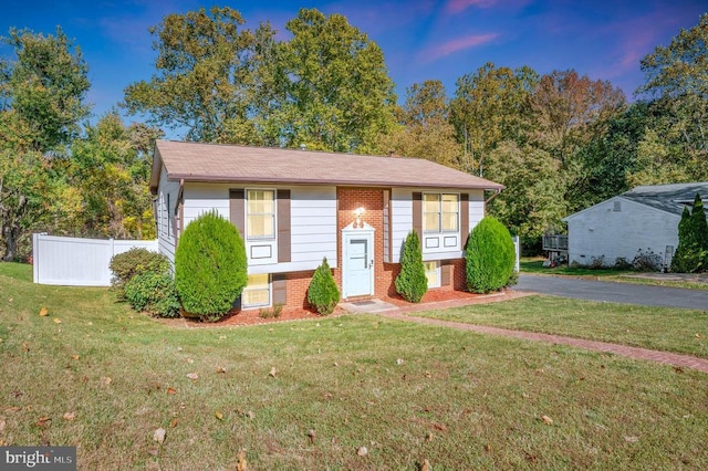 bi-level home featuring brick siding, a front yard, and fence