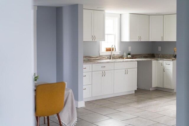 kitchen with light tile patterned flooring, a sink, white cabinetry, and light stone countertops