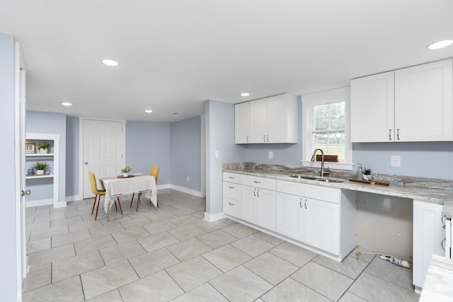 kitchen with baseboards, a sink, light stone countertops, and white cabinets