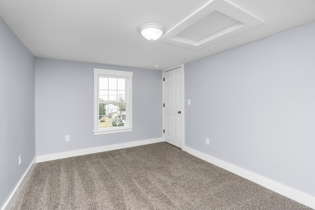 empty room featuring carpet, attic access, and baseboards