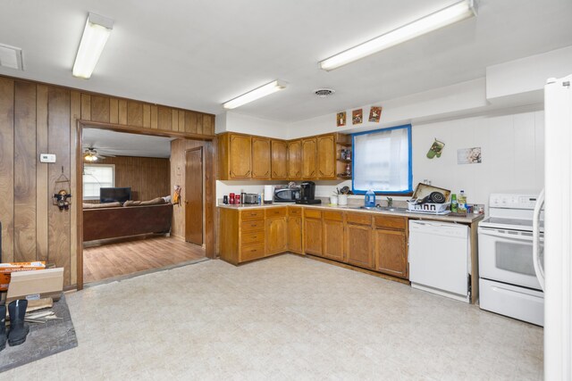 kitchen featuring brown cabinetry, white appliances, wooden walls, and light floors