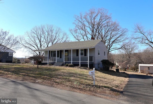 view of front of home with a chimney, covered porch, and a front yard