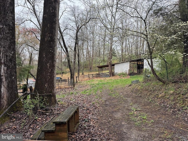 view of yard featuring a forest view, an outdoor structure, fence, and an outbuilding