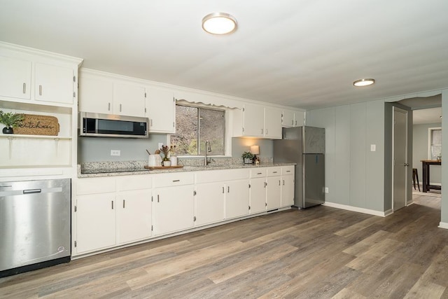 kitchen featuring sink, wood-type flooring, stainless steel appliances, light stone countertops, and white cabinets