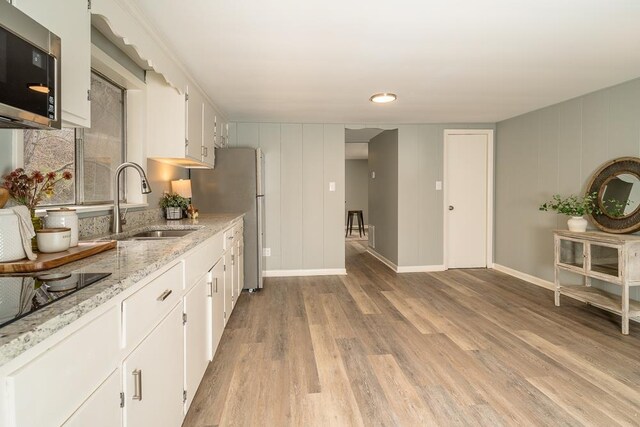 kitchen with sink, light stone counters, black electric stovetop, light hardwood / wood-style floors, and white cabinets