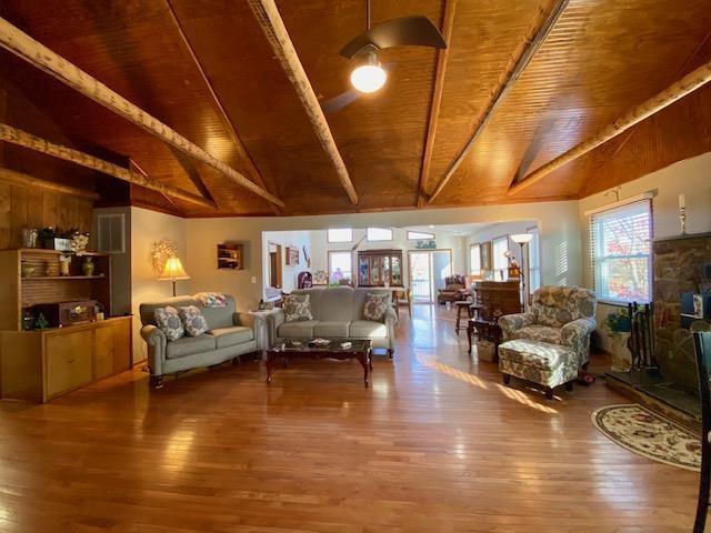 living room with lofted ceiling with beams, wood-type flooring, a stone fireplace, and wooden ceiling