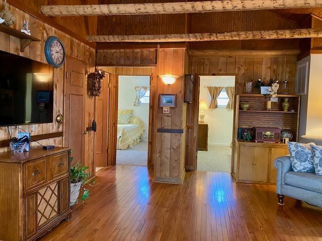 living room with beamed ceiling, wood-type flooring, and wood walls