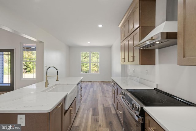 kitchen featuring wall chimney range hood, wood finished floors, a sink, appliances with stainless steel finishes, and recessed lighting