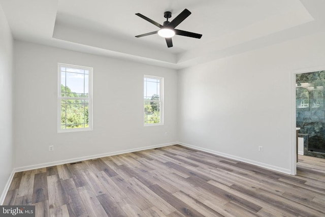 empty room with light hardwood / wood-style flooring, ceiling fan, and a tray ceiling