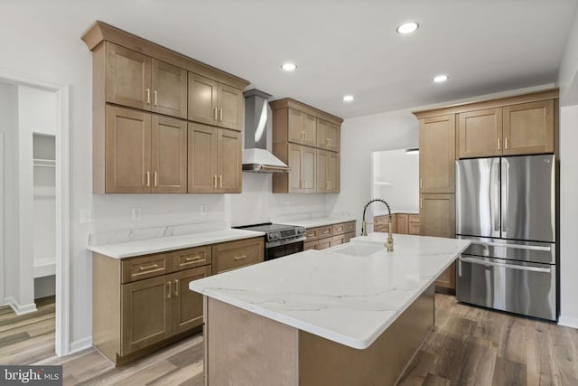 kitchen with light stone counters, wood finished floors, a sink, wall chimney exhaust hood, and appliances with stainless steel finishes
