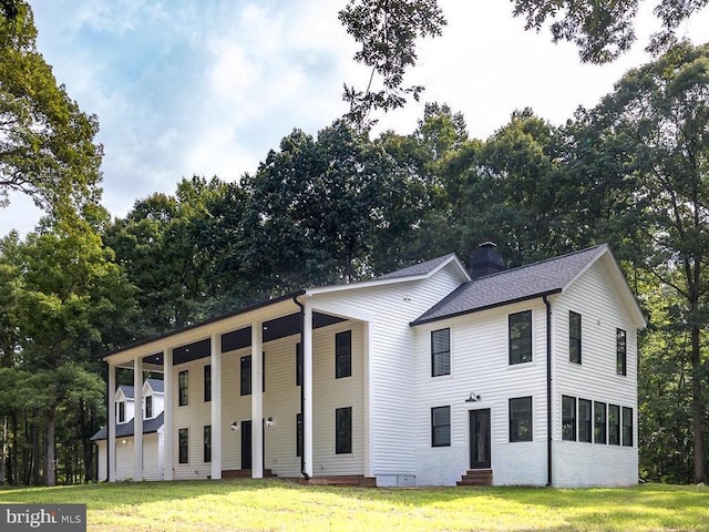 view of front facade featuring entry steps, roof with shingles, a chimney, and a front lawn