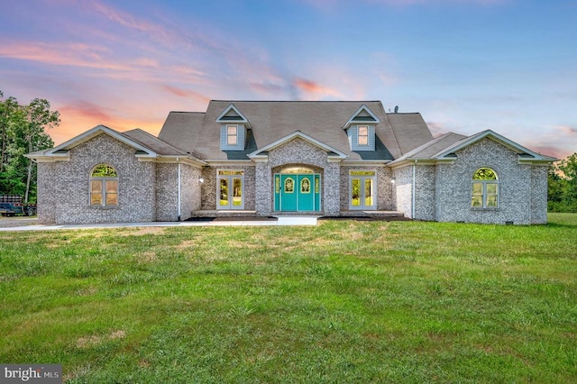 view of front of home featuring french doors, brick siding, and a yard