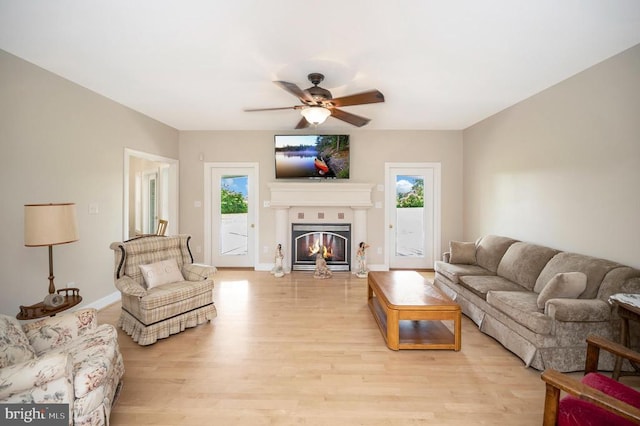 living room featuring light wood-style floors, ceiling fan, baseboards, and a glass covered fireplace