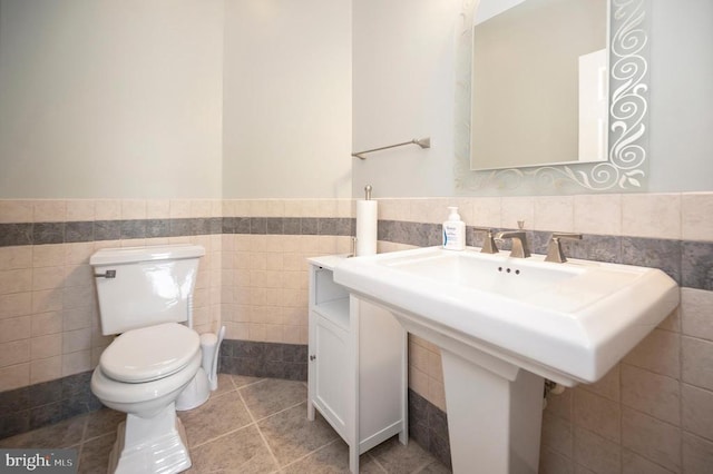 bathroom with toilet, tile patterned flooring, tile walls, and wainscoting