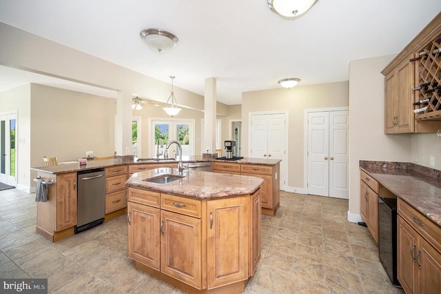 kitchen with stone countertops, baseboards, dishwasher, a kitchen island with sink, and a sink