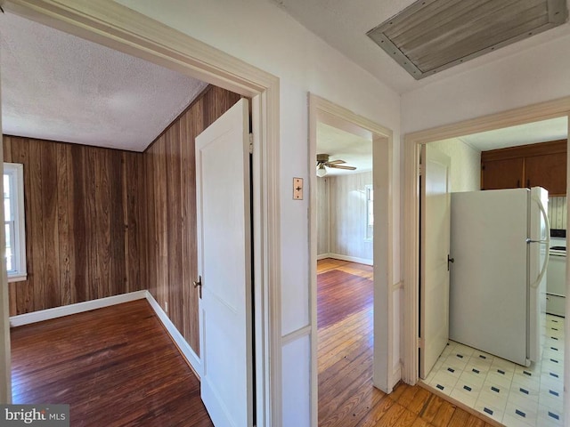 hall featuring light wood-style floors, baseboards, attic access, and wood walls