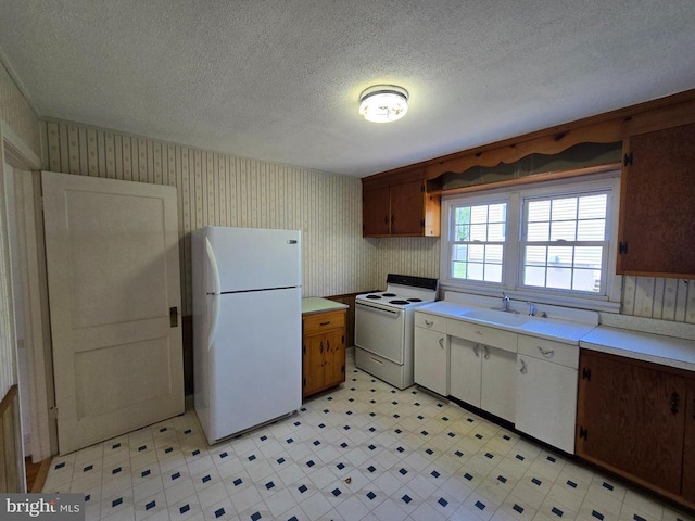 kitchen with a sink, light countertops, light floors, wallpapered walls, and white appliances