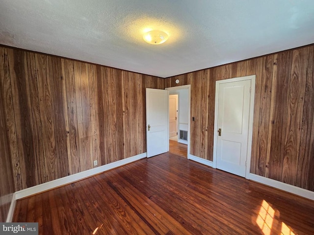 unfurnished bedroom with wooden walls, baseboards, a textured ceiling, and wood finished floors
