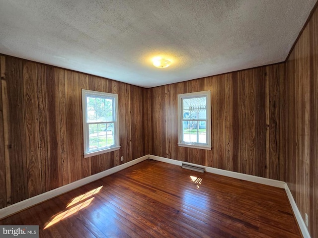 spare room with a textured ceiling, visible vents, a healthy amount of sunlight, and wood finished floors