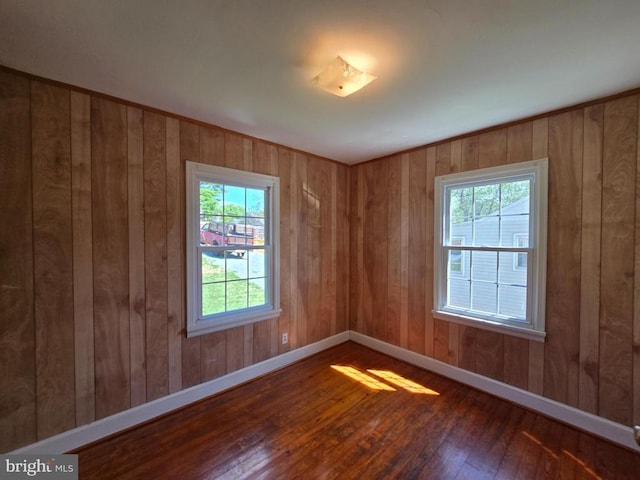 spare room featuring a healthy amount of sunlight, baseboards, hardwood / wood-style flooring, and wooden walls