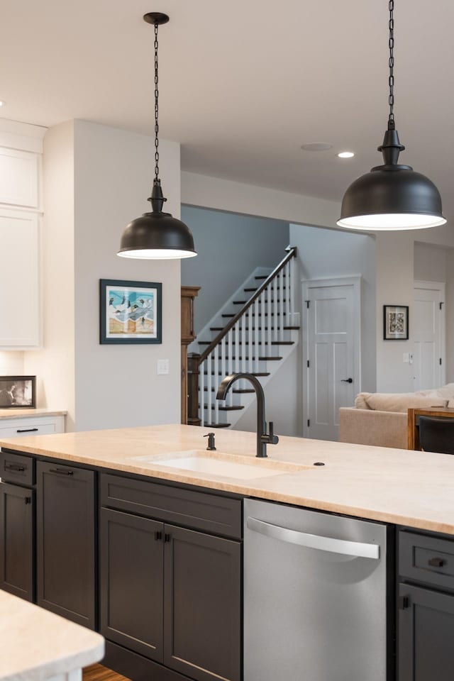 kitchen featuring stainless steel dishwasher, hanging light fixtures, light countertops, and a sink